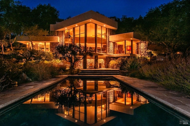 back of house at night with stone siding and an outdoor pool