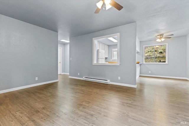 unfurnished living room with baseboards, baseboard heating, and wood finished floors