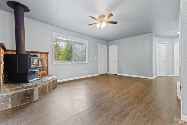 unfurnished living room featuring a wood stove, ceiling fan, baseboards, and dark wood finished floors