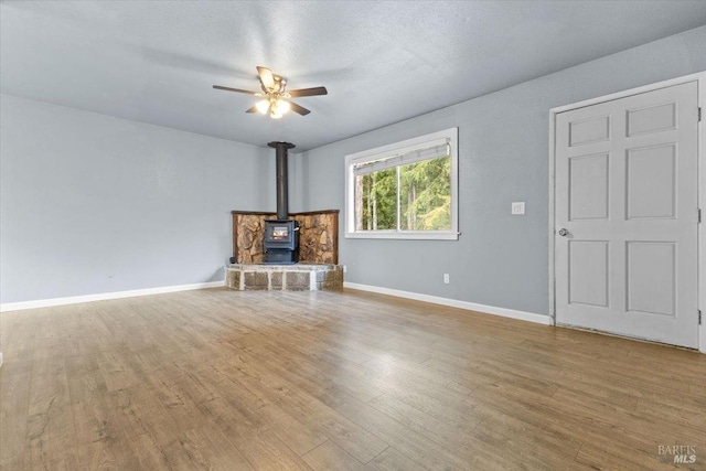 unfurnished living room with a wood stove, ceiling fan, baseboards, and wood finished floors