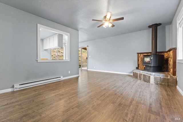 unfurnished living room with a baseboard heating unit, wood finished floors, a wood stove, and baseboards