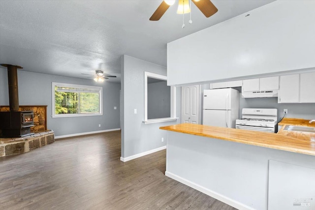 kitchen featuring a wood stove, white cabinets, white appliances, a peninsula, and under cabinet range hood