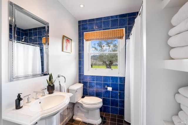 bathroom with tile walls, curtained shower, toilet, a sink, and tile patterned flooring