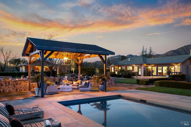 pool at dusk with an outdoor pool, an outdoor bar, a patio, and a gazebo