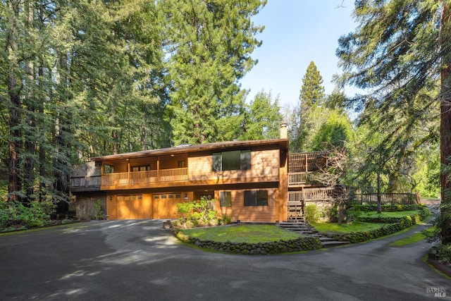 view of front of house featuring aphalt driveway, an attached garage, stairs, a deck, and a front yard