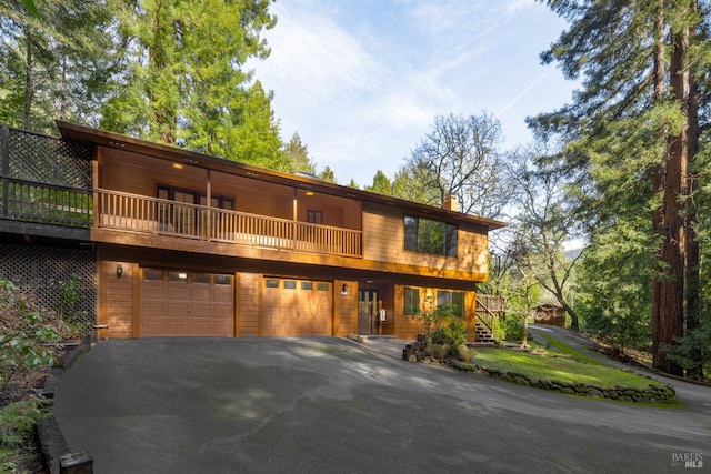 chalet / cabin featuring aphalt driveway, a chimney, and a garage