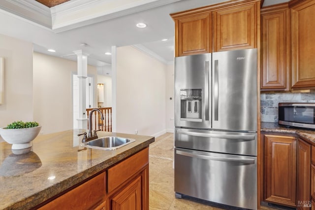 kitchen with stainless steel appliances, ornamental molding, a sink, dark stone countertops, and ornate columns