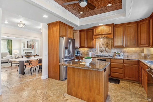 kitchen featuring appliances with stainless steel finishes, a center island, brown cabinetry, and a tray ceiling