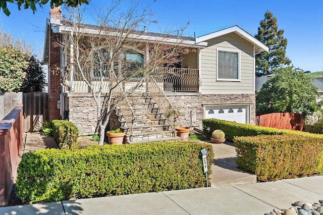 view of front of house featuring an attached garage, stone siding, stairs, and fence