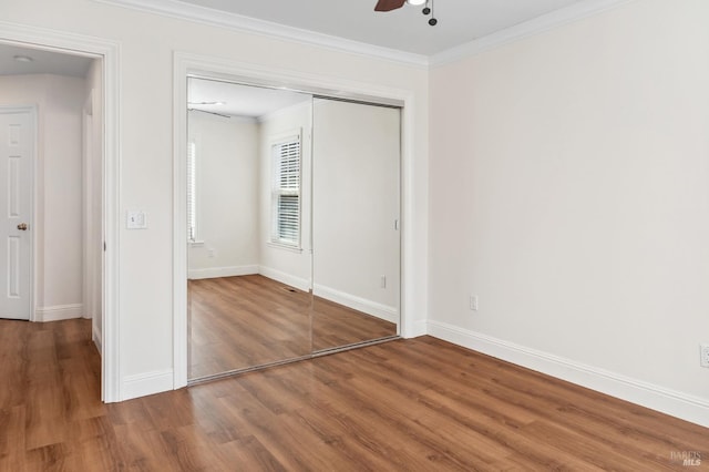 unfurnished bedroom featuring wood finished floors, a ceiling fan, baseboards, ornamental molding, and a closet