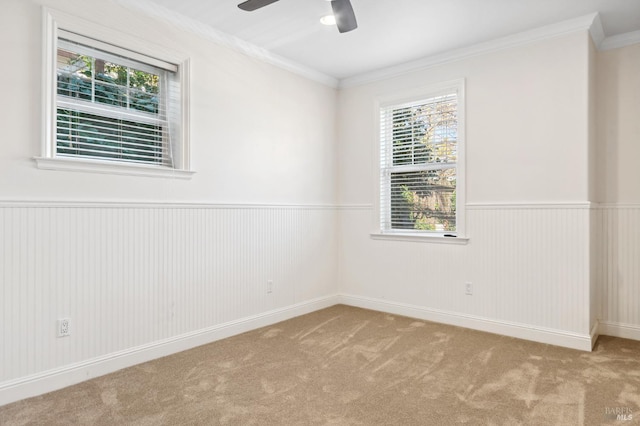 spare room featuring ornamental molding, a wainscoted wall, light carpet, and ceiling fan