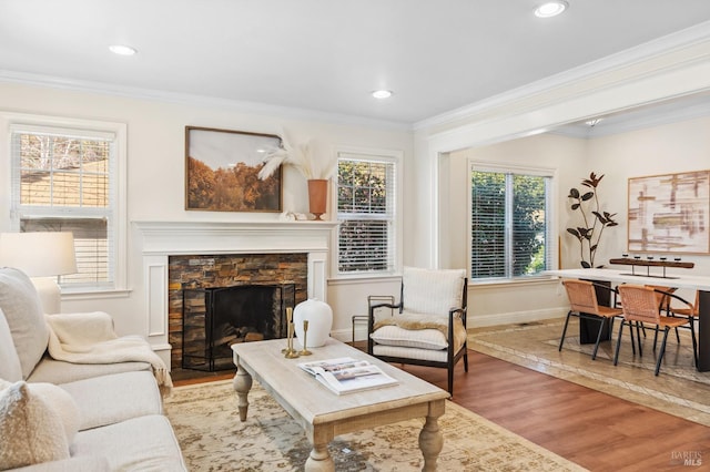 living area with crown molding, a stone fireplace, baseboards, and wood finished floors