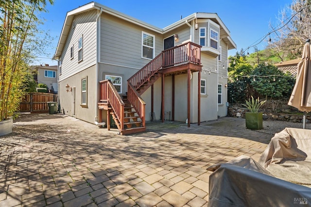 rear view of property featuring stucco siding, stairs, fence, and a patio