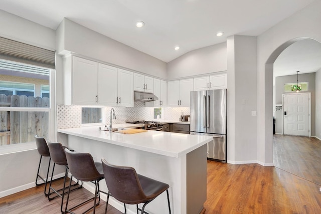 kitchen with a breakfast bar area, stainless steel appliances, backsplash, a peninsula, and under cabinet range hood