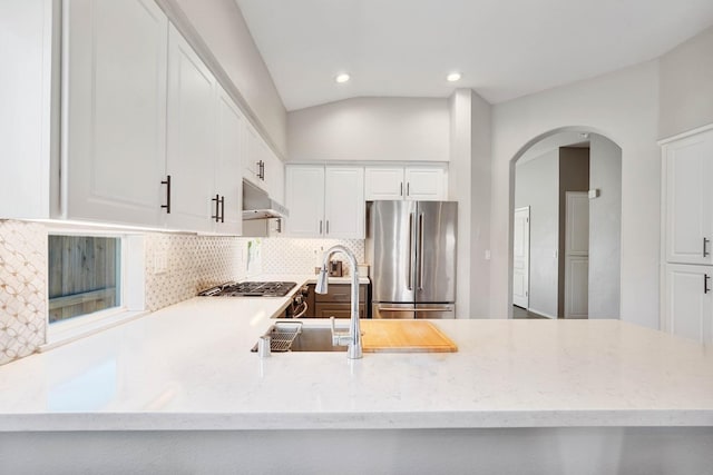 kitchen featuring tasteful backsplash, arched walkways, freestanding refrigerator, light stone countertops, and under cabinet range hood