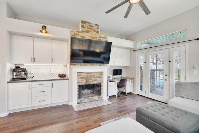 living area with ceiling fan, a stone fireplace, and wood finished floors