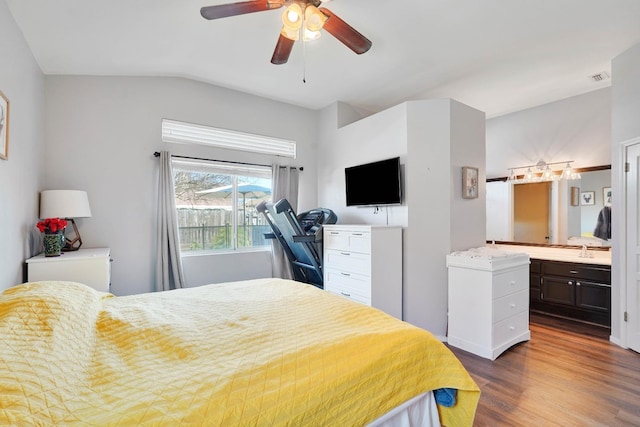 bedroom featuring visible vents, dark wood finished floors, ensuite bathroom, vaulted ceiling, and a sink