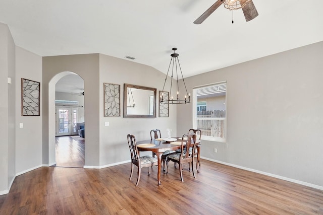 dining space featuring arched walkways, ceiling fan with notable chandelier, wood finished floors, visible vents, and baseboards