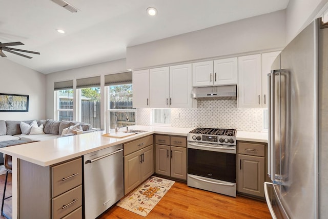 kitchen featuring under cabinet range hood, a peninsula, a sink, visible vents, and appliances with stainless steel finishes