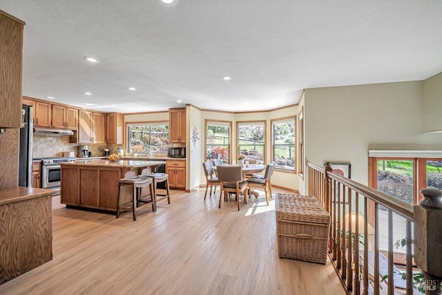 kitchen with black microwave, a kitchen island, stainless steel range with electric cooktop, decorative backsplash, and light wood finished floors