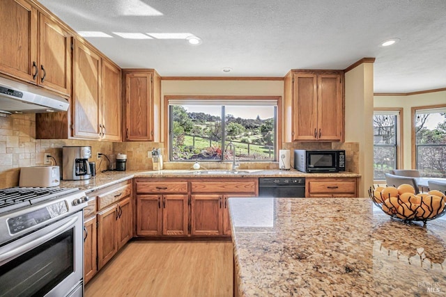 kitchen featuring ornamental molding, light wood-style floors, a sink, under cabinet range hood, and black appliances