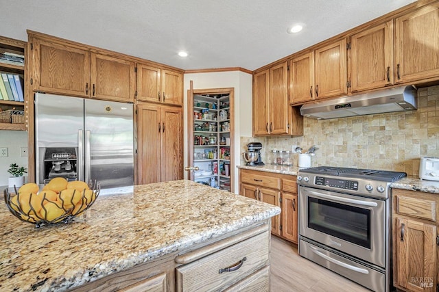 kitchen featuring appliances with stainless steel finishes, backsplash, light stone countertops, and under cabinet range hood