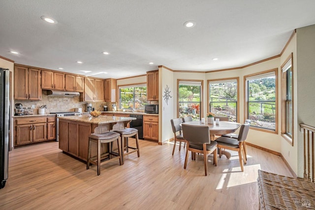 kitchen with a breakfast bar, tasteful backsplash, light wood-style floors, under cabinet range hood, and black appliances