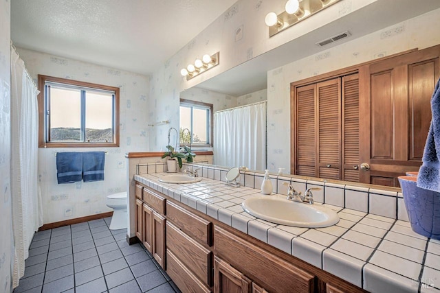 bathroom with toilet, wallpapered walls, baseboards, and a sink