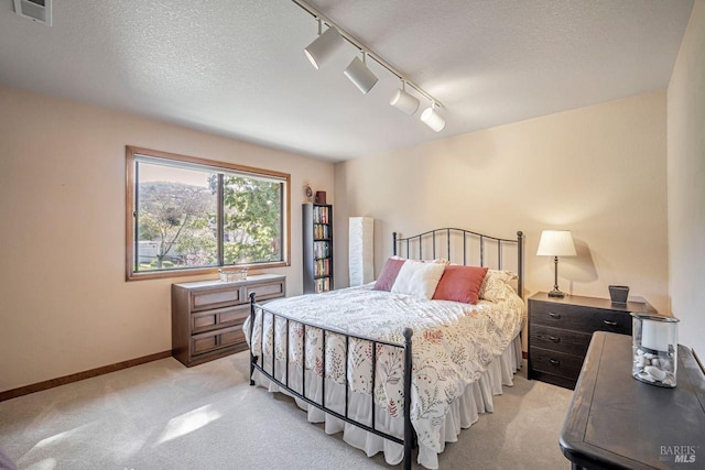 bedroom with rail lighting, visible vents, light carpet, a textured ceiling, and baseboards