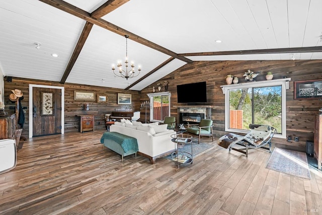 living area with vaulted ceiling with beams, a glass covered fireplace, wooden walls, and wood finished floors