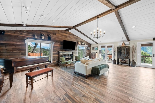 living area featuring a glass covered fireplace, a healthy amount of sunlight, vaulted ceiling with beams, and wood finished floors