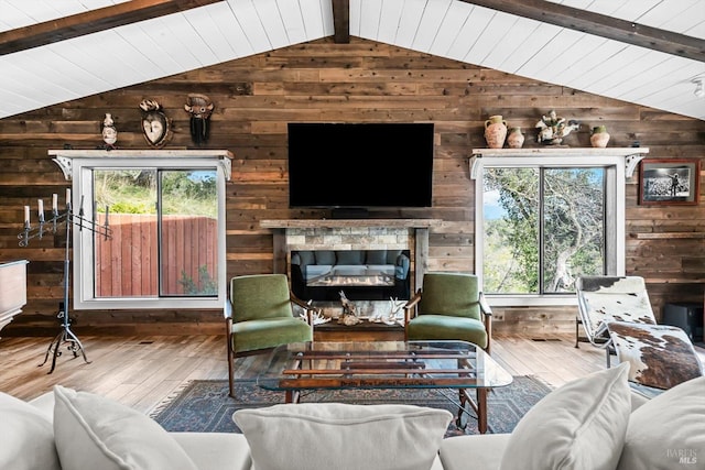 living room with a glass covered fireplace, lofted ceiling with beams, wood-type flooring, wood ceiling, and wood walls