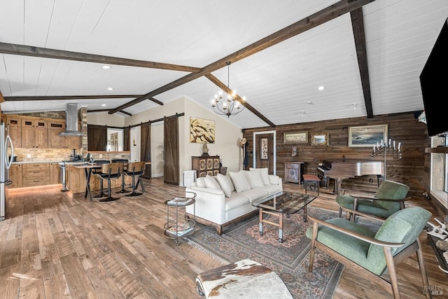 living room featuring lofted ceiling with beams, a barn door, wood walls, wood finished floors, and an inviting chandelier