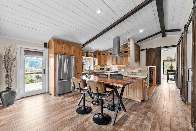 kitchen with a barn door, island range hood, stainless steel appliances, a peninsula, and light countertops