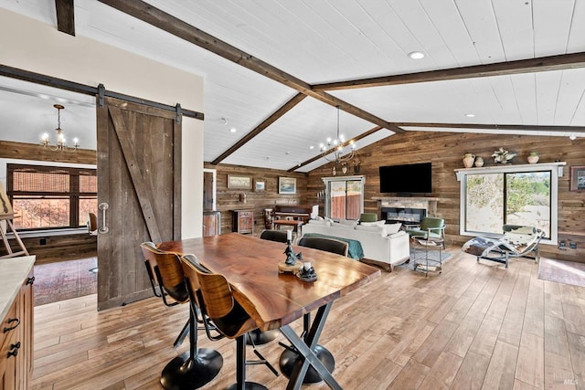 dining room featuring a barn door, wooden walls, light wood-style flooring, vaulted ceiling with beams, and an inviting chandelier