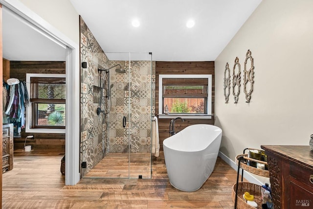 full bath featuring wood walls, wood finished floors, a healthy amount of sunlight, a soaking tub, and a shower stall