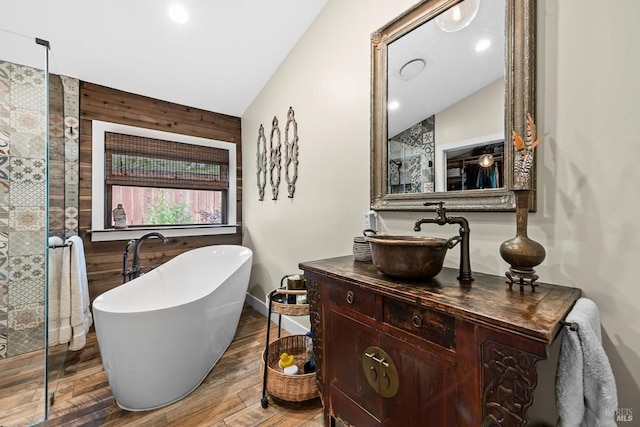 bathroom featuring lofted ceiling, wooden walls, wood finished floors, vanity, and a soaking tub