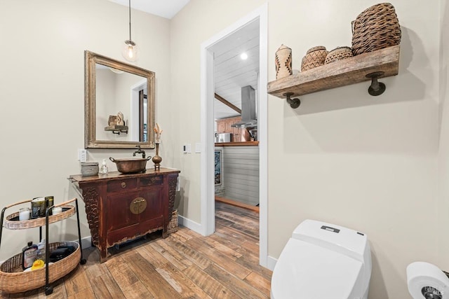 half bath featuring baseboards, toilet, wood finished floors, beamed ceiling, and vanity