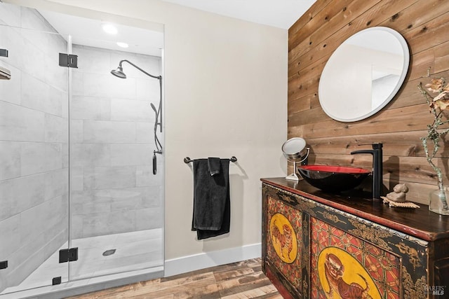 full bathroom featuring wood walls, wood finished floors, vanity, baseboards, and a shower stall