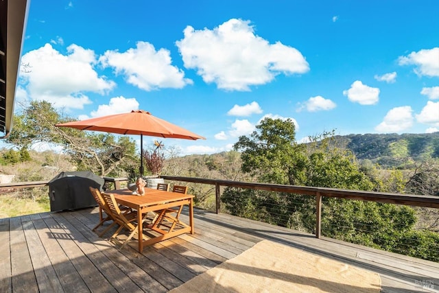 wooden terrace featuring outdoor dining area, grilling area, and a forest view