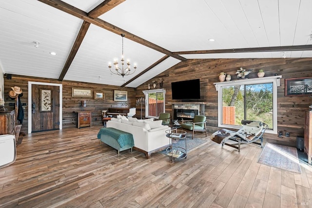 living room with lofted ceiling with beams, a notable chandelier, wood finished floors, and a glass covered fireplace