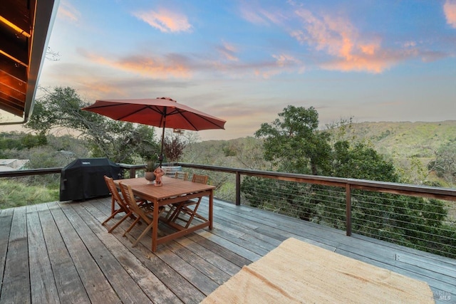 wooden deck featuring outdoor dining space, a grill, and a wooded view