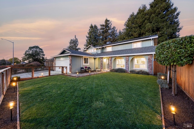 back of house with driveway, a lawn, an attached garage, and a fenced backyard