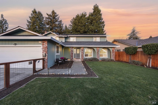 view of front facade featuring an attached garage, fence, a lawn, and roof with shingles