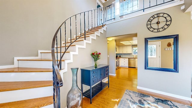 staircase featuring a healthy amount of sunlight, a towering ceiling, baseboards, and wood finished floors