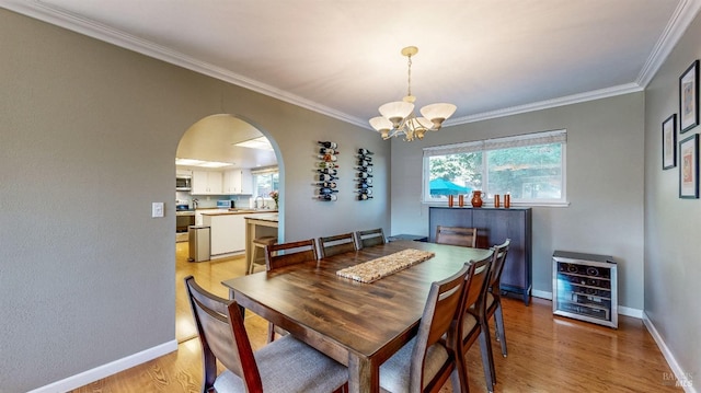 dining room with arched walkways, crown molding, light wood-style flooring, and baseboards