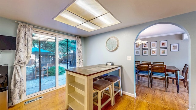 dining area with light wood-type flooring, arched walkways, visible vents, and baseboards