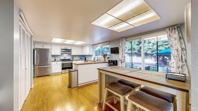 kitchen with stainless steel appliances, a peninsula, a sink, white cabinets, and light wood-type flooring