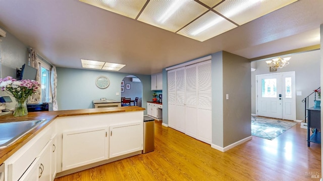 kitchen with arched walkways, light wood finished floors, butcher block counters, white cabinetry, and a sink