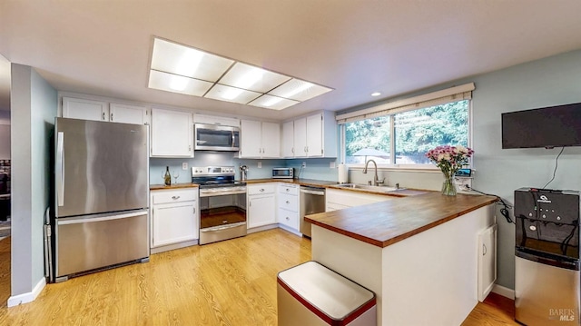 kitchen featuring a peninsula, a sink, light wood-style floors, white cabinets, and appliances with stainless steel finishes